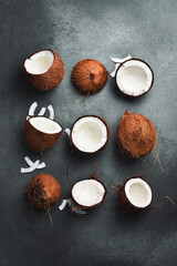 Cracked and whole coconuts on a gray stone background. Top view. Promotional photo.