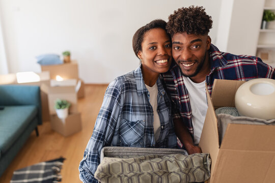 Happy African American couple smiling while unpacking boxes in their new home, enjoying a fresh start together after moving in.