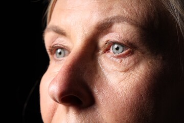 Fototapeta premium Senior woman crying on black background, closeup