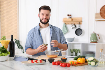 Cooking process. Smiling man seasoning dish at table in kitchen