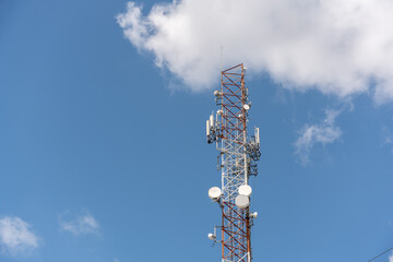 View of a massive telecommunications antenna or transmission tower, supporting various communication antennas for mobile telephony, radio, TV, and internet. The background is a vibrant blue sky.