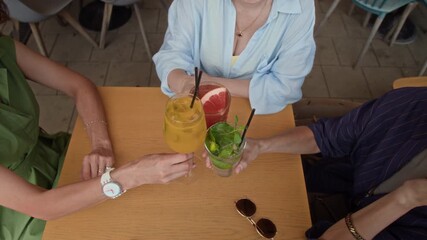 From above view of three mature women sitting at outdoor cafe table, clinking glasses and sipping their cocktail drinks - Powered by Adobe