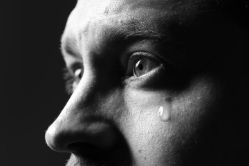 Sad man crying on dark background, closeup. Black and white effect