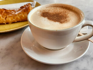 Close-up of a cup of cappuccino with cinnamon on top and a pastry on the side.