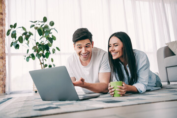 Young couple smiling and bonding over a laptop in a bright modern living room during a cheerful day at home