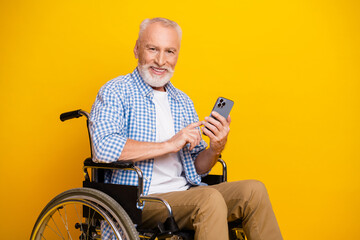 Grandpa on wheels enjoys a sunny selfie moment using a smartphone with a bright yellow backdrop for upbeat rehab and inclusion