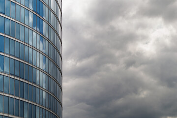 Modern glass office building facade with reflection of cloudy sky