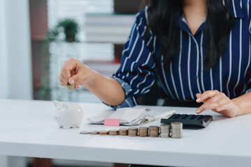 Saving with Vision: A woman meticulously tends to her financial planning, adding a coin to her piggy bank. This captures the essence of thoughtful saving and financial prudence. © Kritdanai