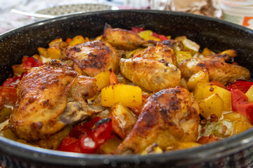Close, shallow-depth image of roasted chicken pieces with peppers and potatoes in a pan; crispy skin and caramelization visible. Great for culinary promotion, recipe cards and food advertising.