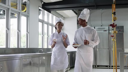 African American male and female chefs walking together in a commercial kitchen, discussing recipes and smiling while preparing food during teamwork.