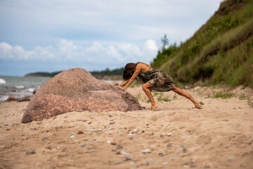 A determined woman is seen energetically pushing a large, heavy rock on a sandy beach with a...