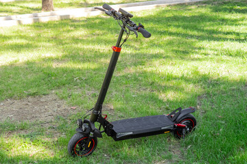 Black electric scooter with red accents parked on grassy surface, scooter concept