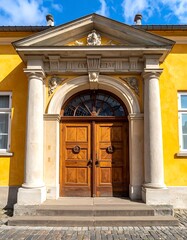 Obraz premium A grand wooden double door with arched glass leads into a sun-drenched yellow building, framed by white pillars