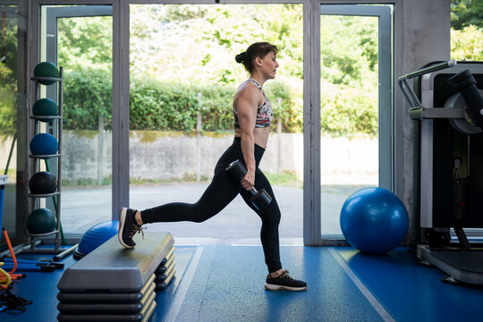 Woman exercising with dumbbells, training legs in gym