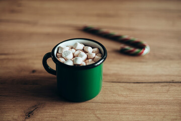 Green metal cup with hot chocolate and marshmallows on a wooden table.
