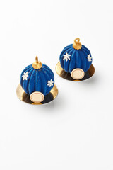 Two blue christmas mousse cakes resembling christmas baubles with golden tops and white snowflakes decoration on golden bases