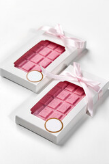 Two pink chocolate bars wrapped with pink ribbon in white box on white background