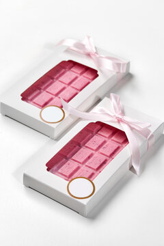 Two pink chocolate bars wrapped with pink ribbon in white box on white background