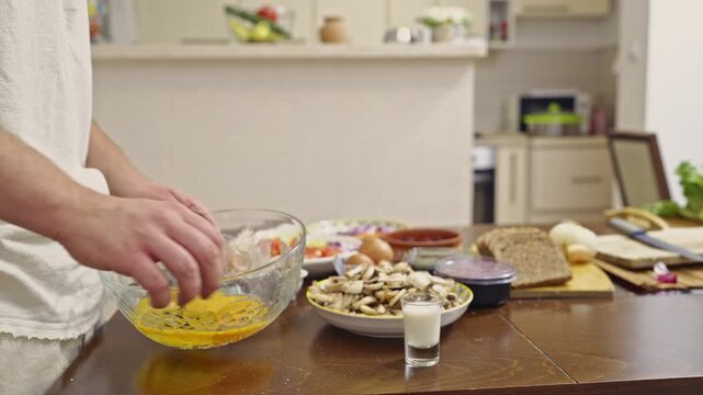 Watch as a person cracks eggs into a bowl and whisks them with milk, preparing a delicious homemade breakfast. Experience the authentic sounds of cooking in this detailed 4K footage.