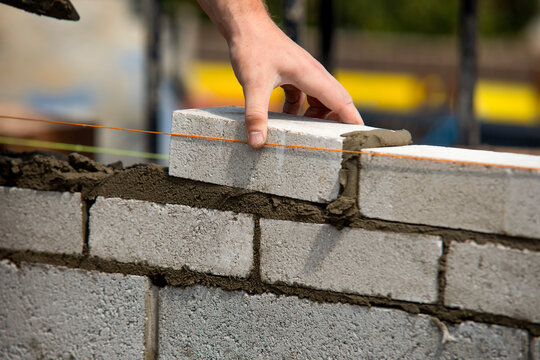 Bricklayer carefully places a concrete block while constructing a sturdy wall using precise techniques in bright daylight