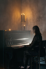 Elegant woman in black lace dress playing piano by candlelight in a moody, gothic atmosphere