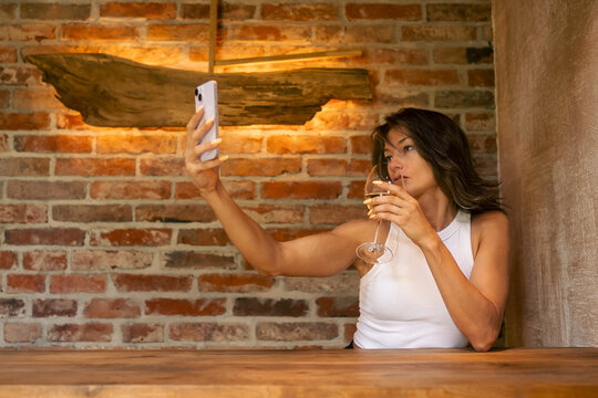 In a cozy and rustic interior, a stylish woman enjoys sipping her drink and taking an adorable selfie