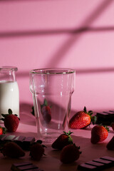 Pink background with empty glass and strawberries