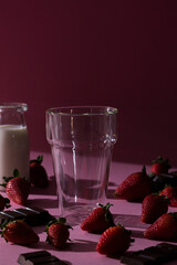 Pink background with empty glass and strawberries