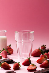 Pink background with empty glass and strawberries