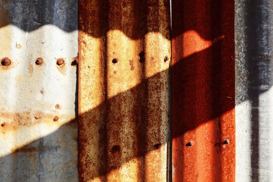 Weathered corrugated metal panels with rivet details, illuminated by light and shadow - Powered by Adobe