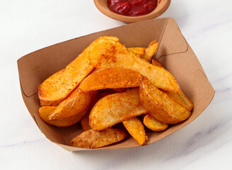 Crispy Baked Spicy Potato Wedges Seasoned with Paprika, Served in a Cardboard Tray on marble background closeup view of fast food