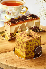 Delicious modern cakes with gold decorations resting on wooden table near teacup