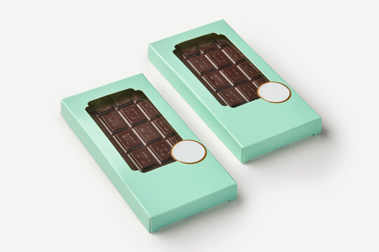 Two dark chocolate bars resting in light green boxes on white background