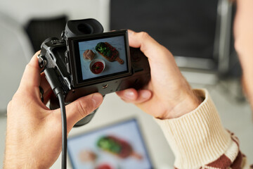 Man holding digital camera photographing food on table, hands visible adjusting settings, capturing...