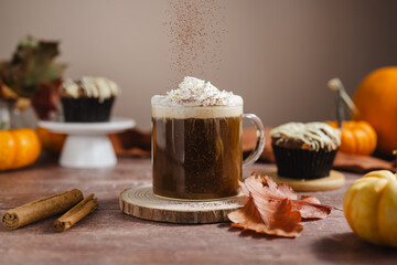Pumpkin spice latte in glass mug with whipped cream and cinnamon, autumn hot drink