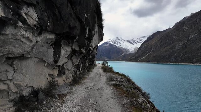 Huaraz, Peru: Point of view of a traveler walking on the trail by laguna paron in Huaraz, Peru. Located in Cordillera blanca mountain with dramatic sky over snowcaped Piramide mountain peak 