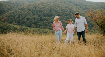 Family enjoys a walk in a grassy field surrounded by mountains during a sunny afternoon