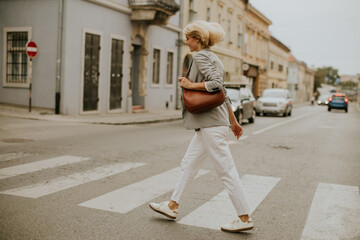 Woman crossing the street in a city wearing casual clothes and carrying a bag