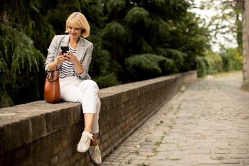 Woman sitting on stone wall in a park while using smartphone during a sunny day in the afternoon