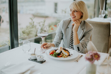 Elegant woman enjoying fine dining at a modern restaurant while sipping wine and savoring gourmet food on a sunny day
