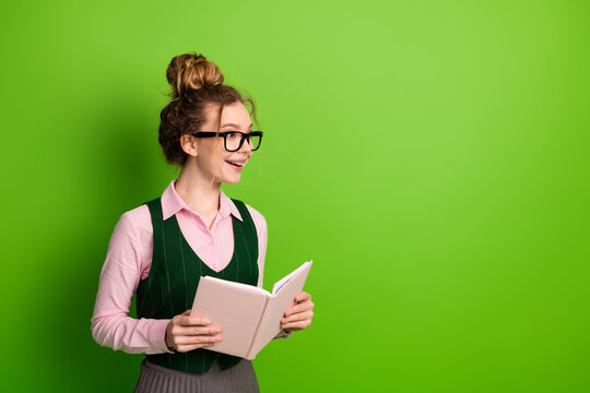 Young student holding a book against green background, wearing glasses, learning and smiling with happy expression