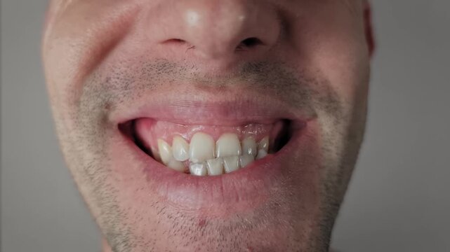 Extreme close up shot of an unshaven male face puckering lips for a kiss then relaxing. The shot shows pink lip texture and dark stubble against a neutral grey studio background.