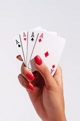 Female hand with red nail polish holding four aces from a standard deck of playing cards isolated on bright neutral background. Copy space, aspect ratio 9:16