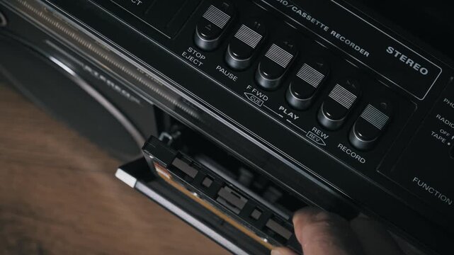 Top down shot of a hand ejecting and removing a vintage cassette tape from a boombox player then re inserting it into the deck closing the door and pressing the play button