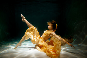 A graceful and elegant underwater dance performance draped in a flowing yellow dress