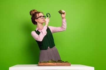 Young woman wearing glasses studying plants with a magnifying glass in a school setting on a green background
