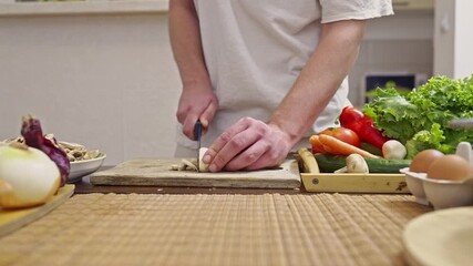 Men slices fresh mushrooms on a wooden cutting board, preparing a healthy meal with an array of vibrant vegetables and eggs in a clean kitchen environment, complete with authentic cooking sounds. - Powered by Adobe