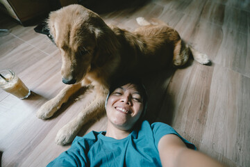 A real Asian man takes a selfie with a year-old golden retriever. The dog is licking its owner's face. Smiling People and fun playing together looking happily at the camera at home Pet and person