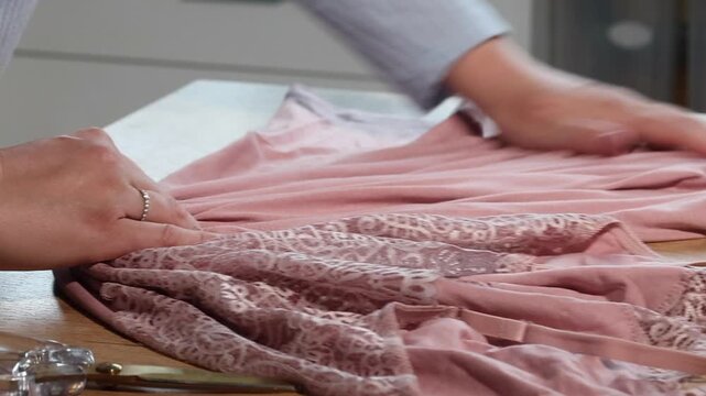 A woman is reviewing a pink lace nightgown. She is laying it out on the table_