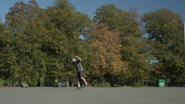 A skateboarder doing tricks in slow motion in a basketball pitch in the sunset